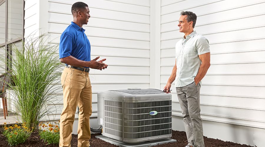 HVAC technician discussing energy-efficient upgrades with homeowner next to new air conditioning unit, promoting benefits of the Inflation Reduction Act.