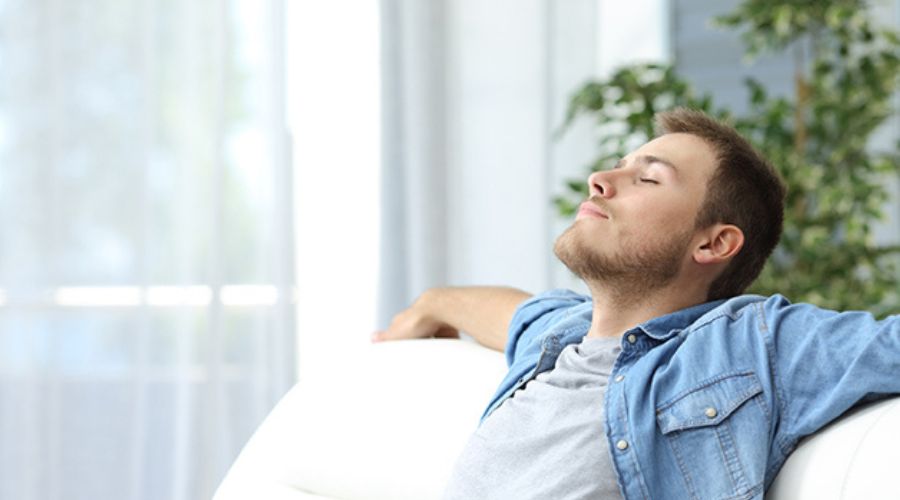 Man relaxing on a couch, enjoying fresh air indoors, representing comfort and breathing easier during spring allergy season.