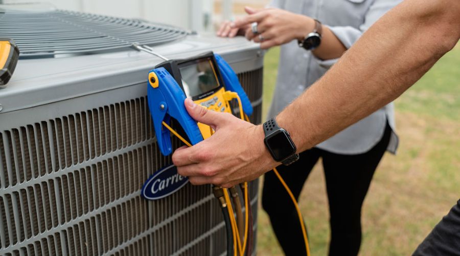 Technician servicing a Carrier air conditioning unit with diagnostic tools, emphasizing HVAC maintenance and energy efficiency.