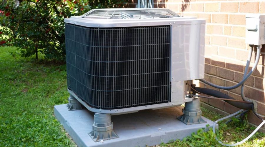 Air conditioning unit on a concrete pad in a green lawn, emphasizing the importance of spring maintenance for HVAC systems.