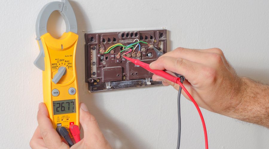 Technician testing thermostat connections with multimeter for HVAC maintenance and replacement.