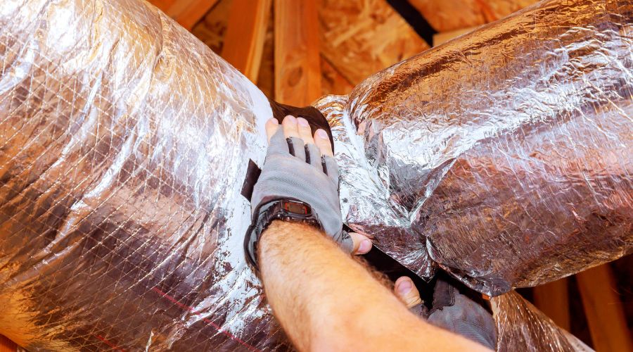 Person inspecting and repairing damaged ductwork in an attic, highlighting the importance of air duct maintenance for improved indoor air quality and HVAC efficiency.